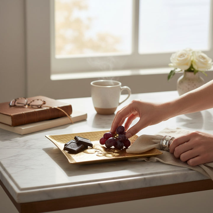  The gold-toned hammered aluminum fleur-de-lis plate elegantly styled on a living room coffee table as a chic decorative catch-all.