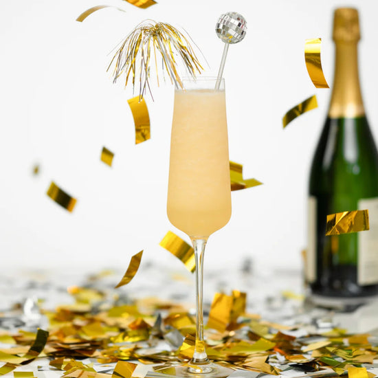 Champagne flute with a cocktail and bottle of champagne on a table with confetti.