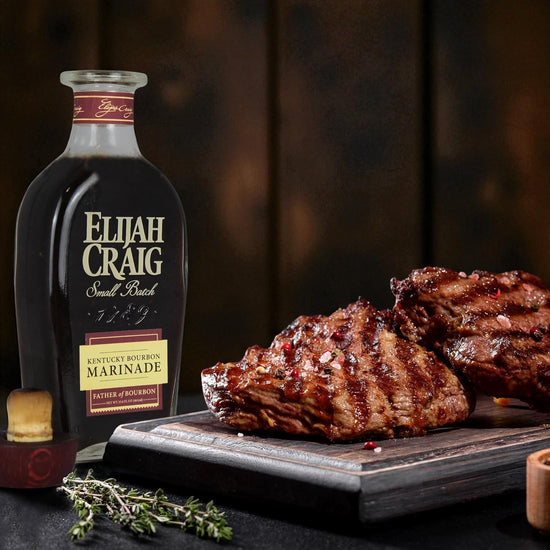 Bottle of Elijah Craig bourbon marinade with marinated meat on a wooden board.