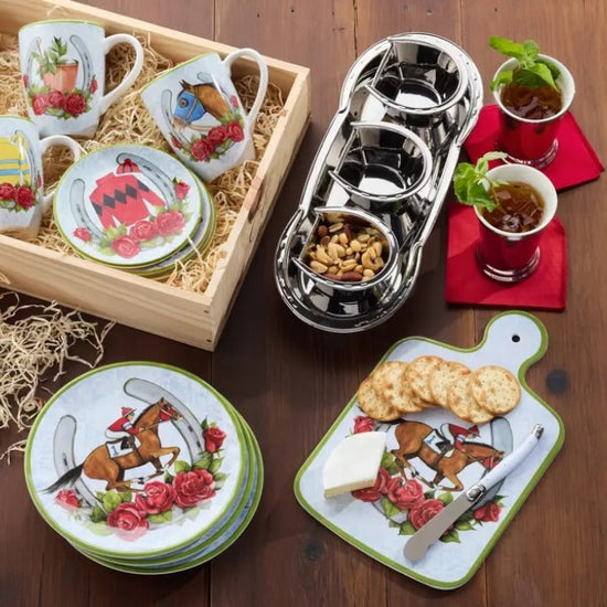 A lifestyle image showing the "Day at the Races" cheese board arranged with various cheeses, crackers, and nuts on a wooden table during a festive gathering.