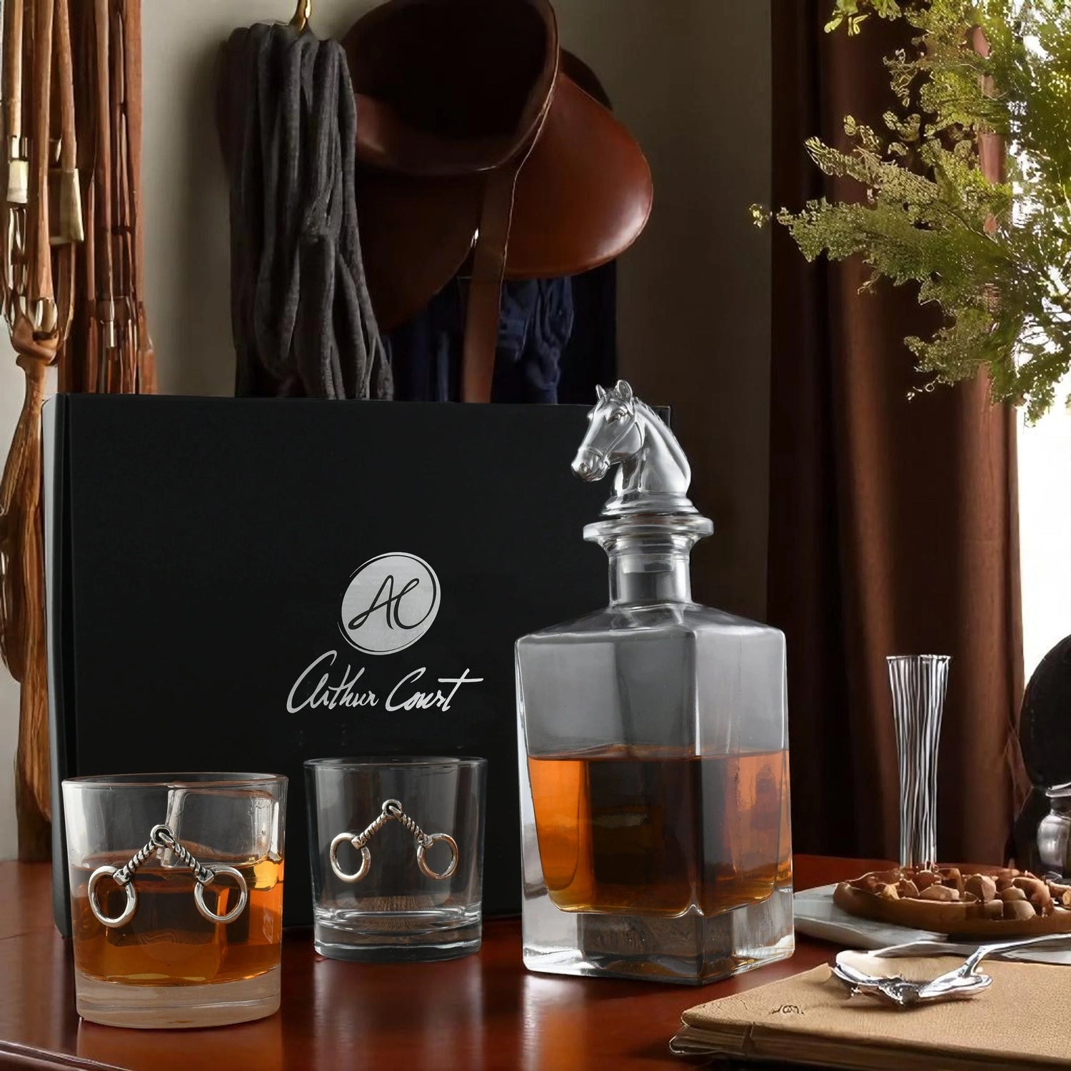 Whiskey decanter and glasses with 'Arthur Court' branding on a wooden table.