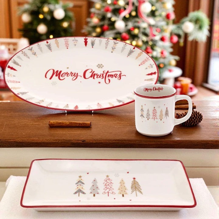 A lifestyle shot showing the Festive Trees mug and plates arranged on a holiday table with festive decor.