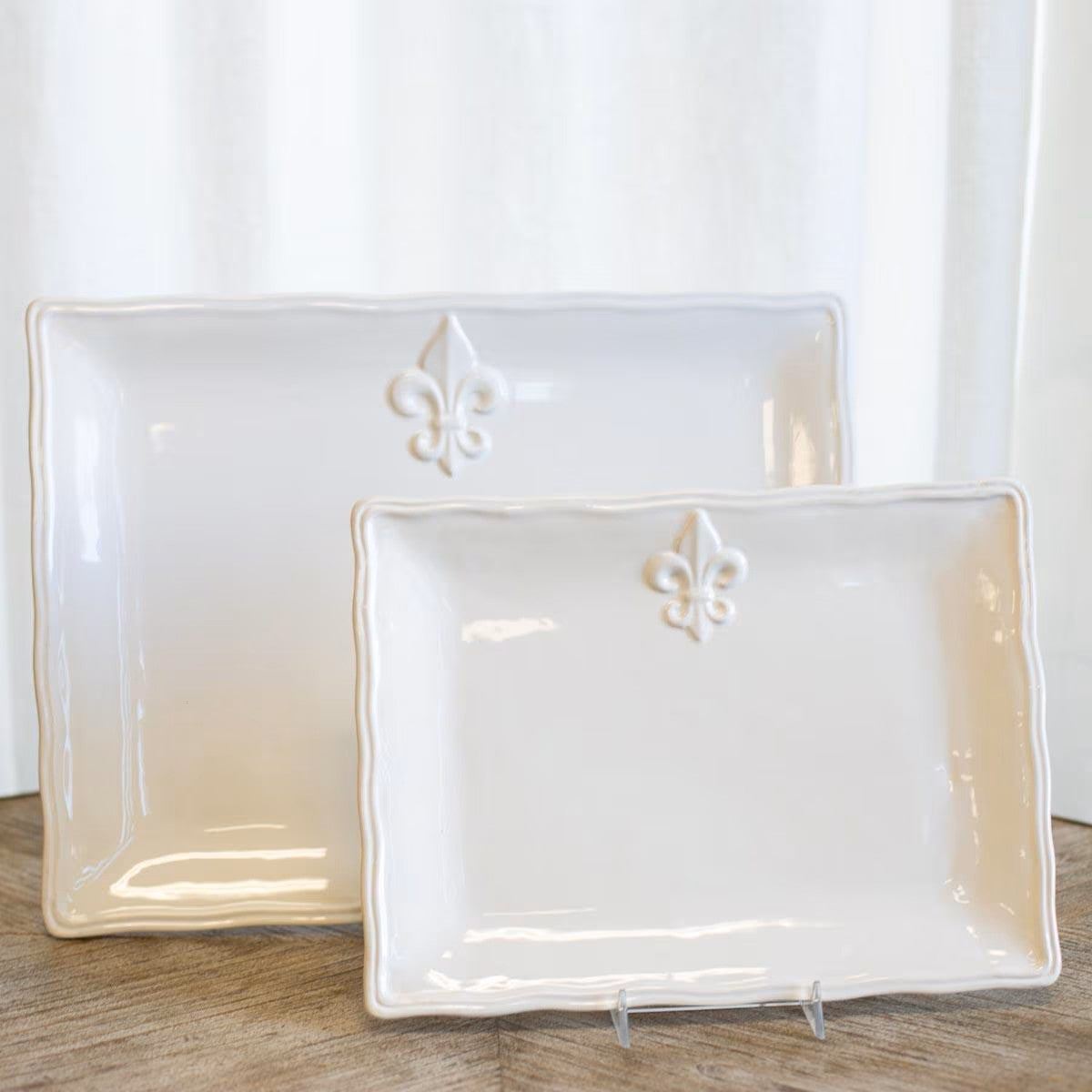 Two white ceramic trays with fleur-de-lis designs on a wooden surface.