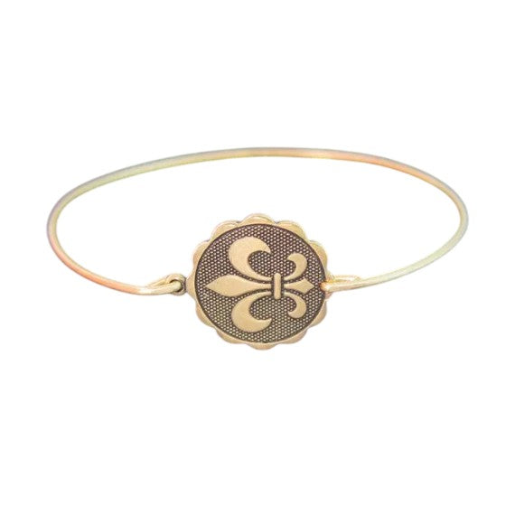 A gold-tone bangle bracelet with a round fleur de lis coin charm on a white background.
