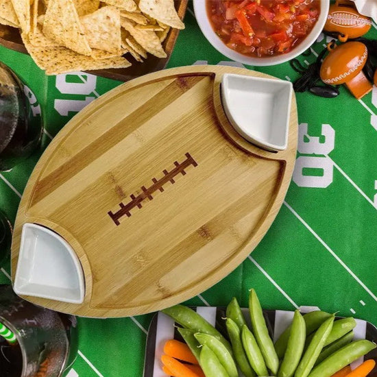 Wooden football-shaped cutting board with two white compartments on a sports-themed table.