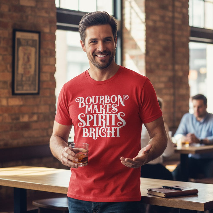 Man wearing a red t-shirt with text,  Bourbon Makes Spirits Bright, holding a glass in a casual setting.