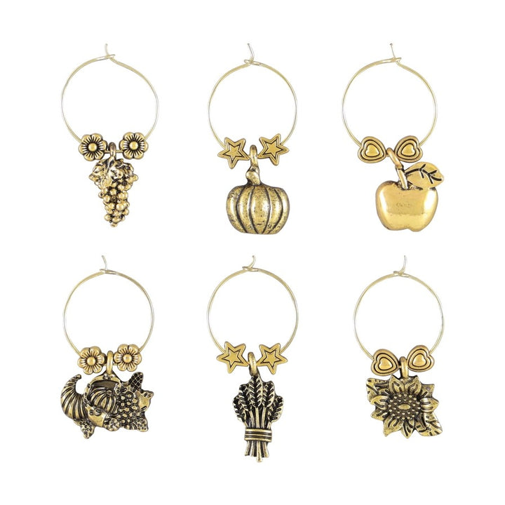 Flat lay of six harvest-themed wine charms—grapes, pumpkin, apple, cornucopia, wheat, sunflower—on white background.