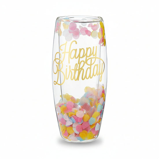A clear, stemless double-wall champagne glass filled with colorful pastel confetti and featuring "Happy Birthday" in gold script.