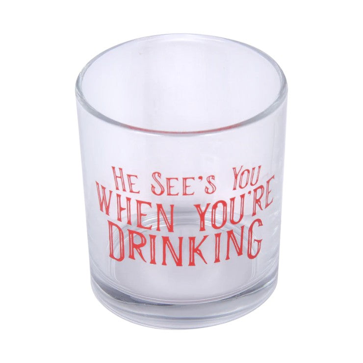 Clear glass with red text 'He sees you when you're drinking' on a white background