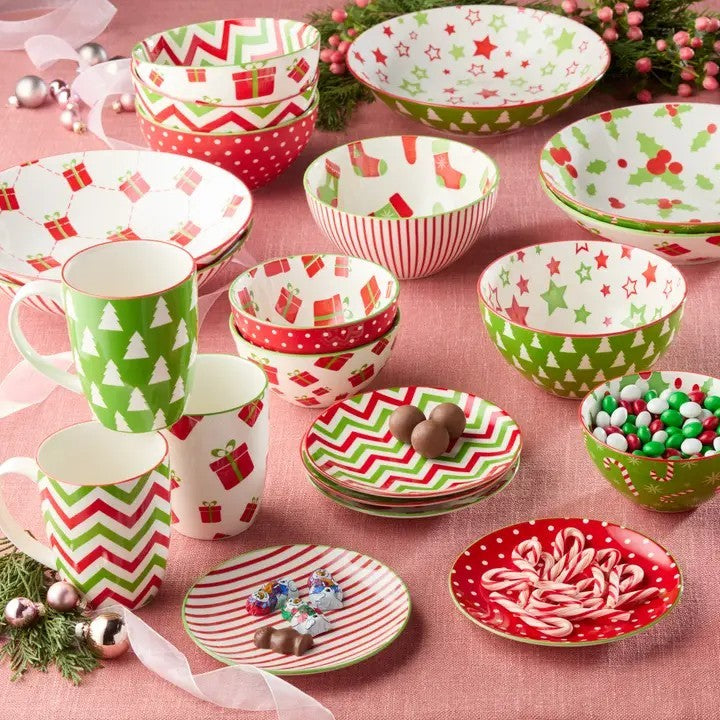Set of Christmas-themed mugs, bowls, and plates on a pink tablecloth.