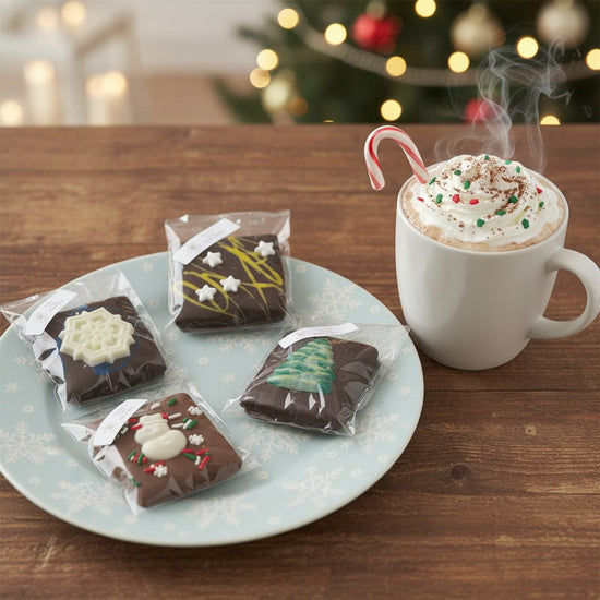 A single decorated chocolate graham cracker on a plate next to a mug of hot cocoa.