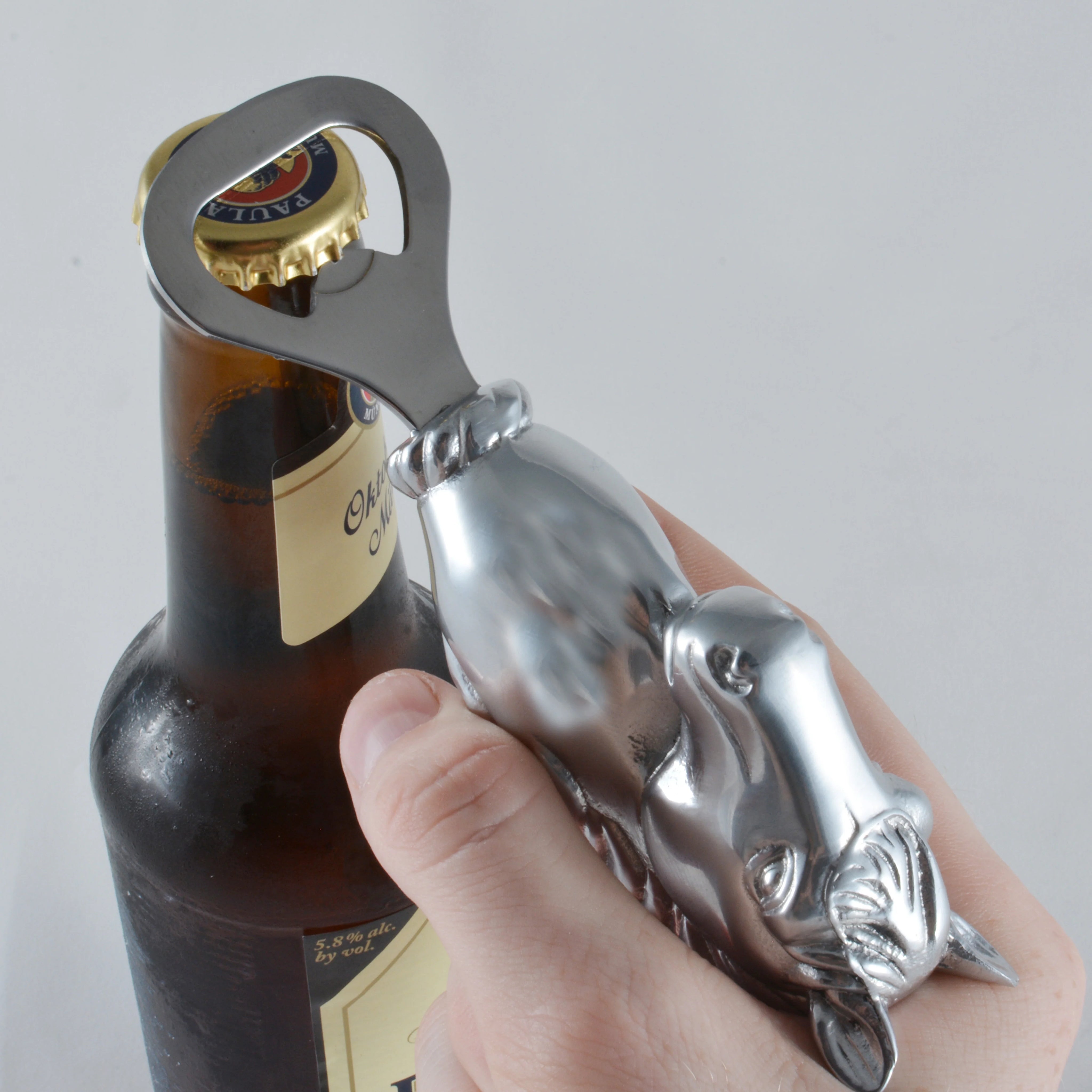 Metal bottle opener shaped like a dog being used on a bottle.