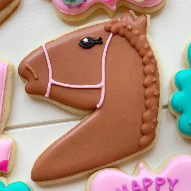 Decorative cookie shaped like a horse head with pink details on a white surface.