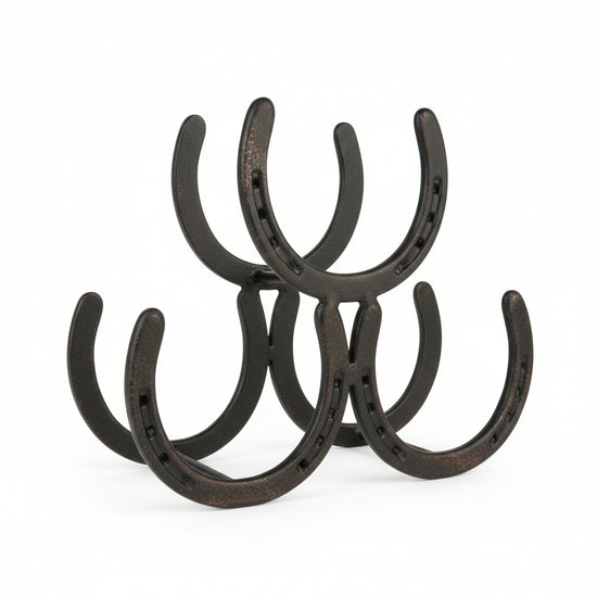 A rustic metal wine rack made of interconnected horseshoes holding three wine bottles on a kitchen counter.