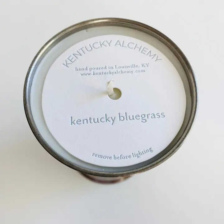 Candle lid with 'Kentucky Alchemy' branding and 'Kentucky Bluegrass' scent on a white background
