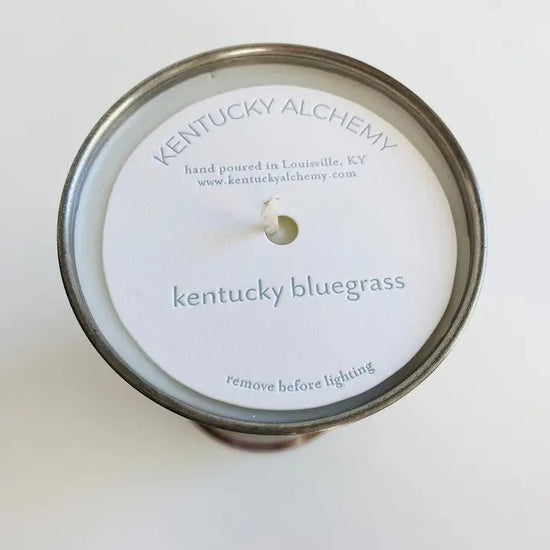 Candle lid with 'Kentucky Alchemy' branding and 'Kentucky Bluegrass' scent on a white background