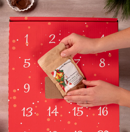 Hand opening a red Kentucky Advent Calendar to reveal a small bag of Jingle Bello Java coffee.