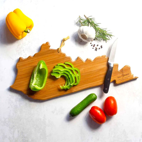Wooden cutting board with knife, sliced green pepper, and various vegetables on a white background