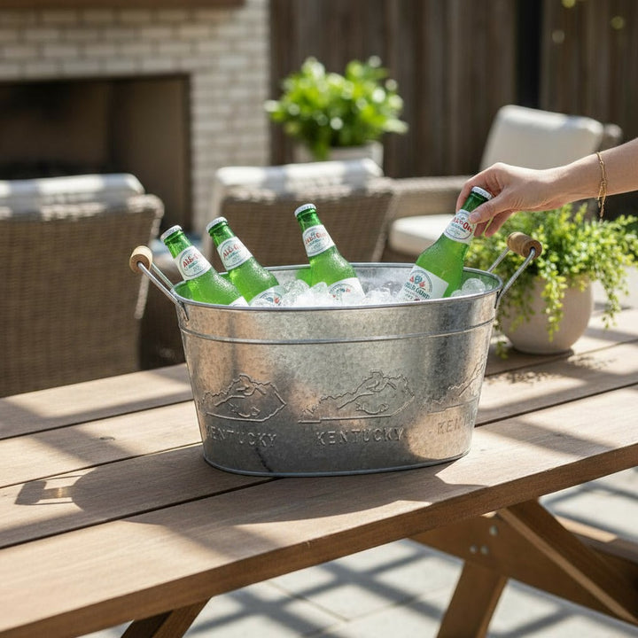 A galvanized beverage tub with an embossed Kentucky design filled with ice and bottles on a patio.