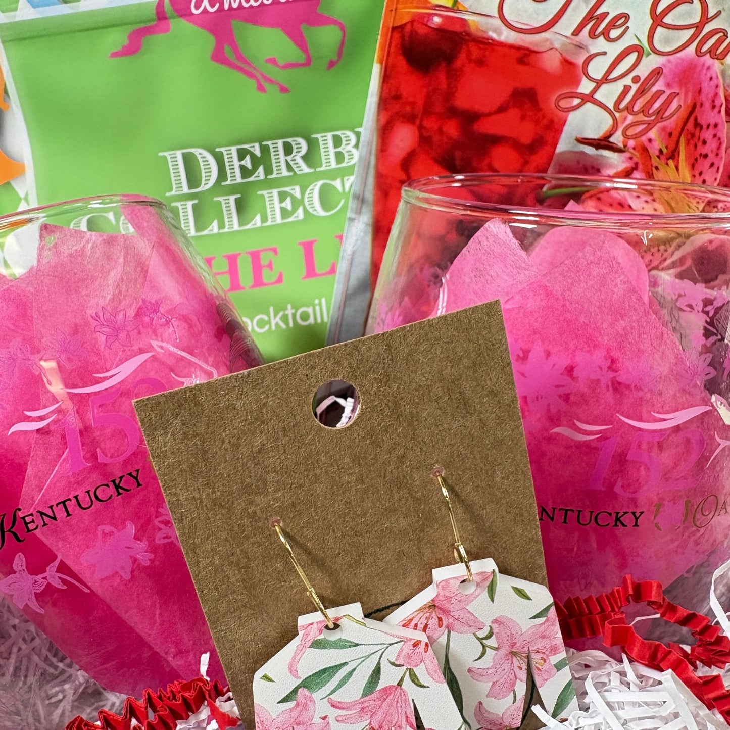Two official 152nd Kentucky Oaks stemless glasses filled with pink tissue next to a pouch of d'marie The Lily cocktail mix.