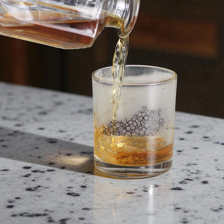 Alcohol being poured from a decanter into a glass on a speckled countertop.