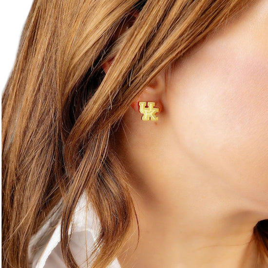 Gold earrings with 'UK' symbol worn by a person with brown hair.