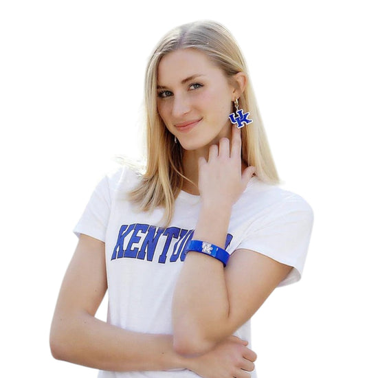 Woman wearing a white shirt with 'Kentucky' text, blue earrings, and bracelet on a white background