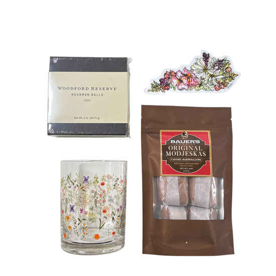 Top-down view of the gift basket contents: Boho Flower Rocks Glass, wildflower sticker, bourbon balls, and Modjeskas.