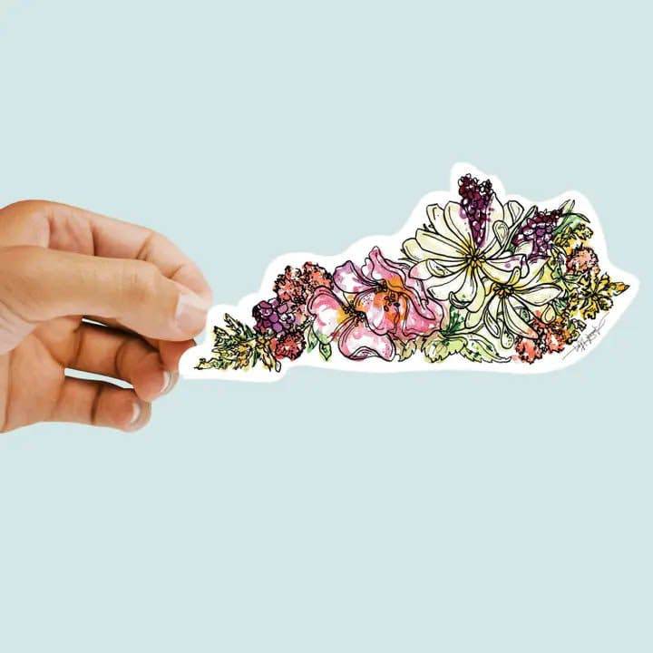 Hand holding a floral-shaped sticker against a light blue background