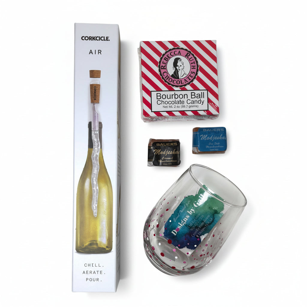 A top-down view of the gift basket contents: a wine chiller, Gail Corso wine glass, a bourbon ball, and two Modjeskas.