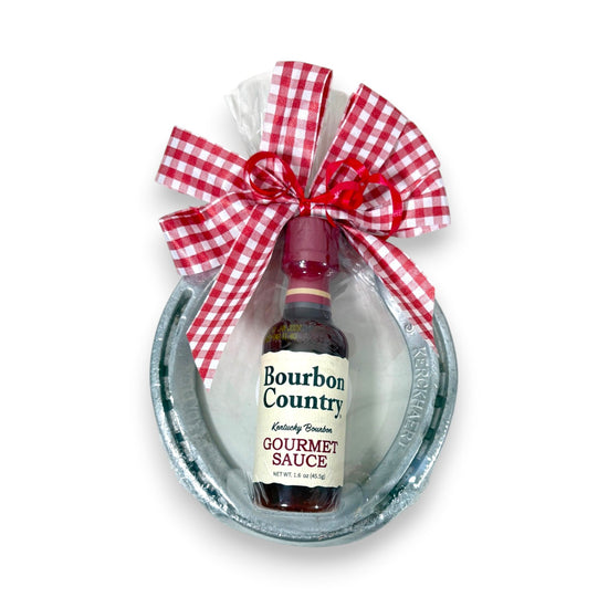 Authentic Churchill Downs horseshoe topped with a mini bottle of Bourbon Country Gourmet Sauce, tied with a gingham bow on a white background.