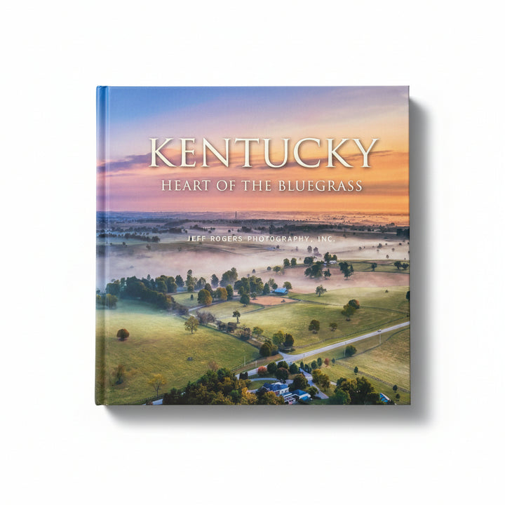Front cover of Kentucky: Heart of the Bluegrass features an aerial view of rolling green hills, winding roads, and a vibrant sunrise sky.