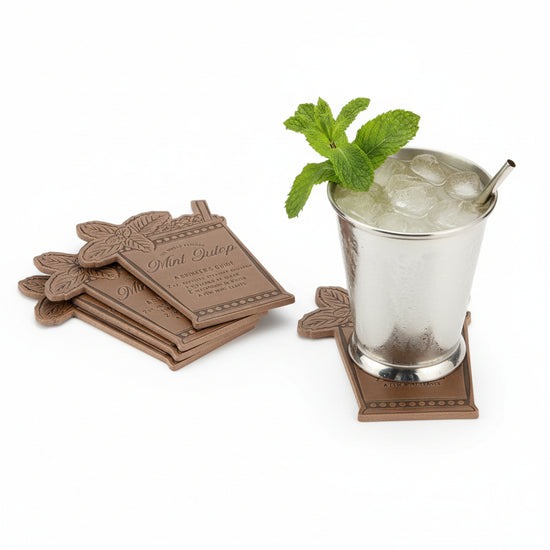 A silver julep cup filled with mint and ice resting on a brown leather coaster that displays the Mint Julep recipe.