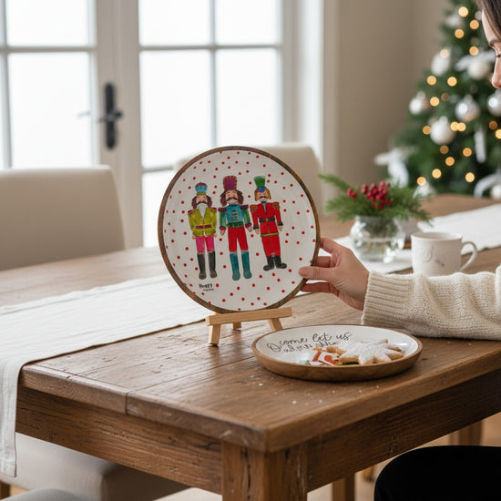 Person holding a decorative plate with Christmas-themed design on a wooden table.