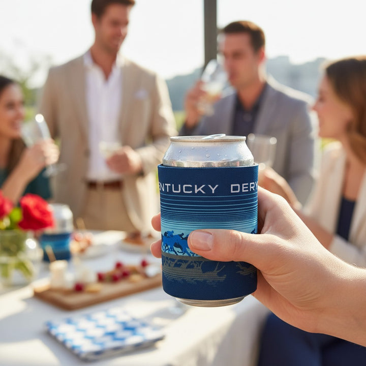 Person holding a can with a Kentucky Derby-themed koozie at an outdoor gathering.