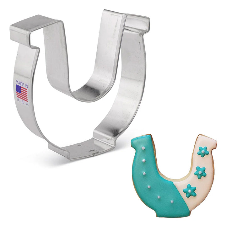 Metal horseshoe cookie cutter with a decorated cookie shaped like a horseshoe on a white background