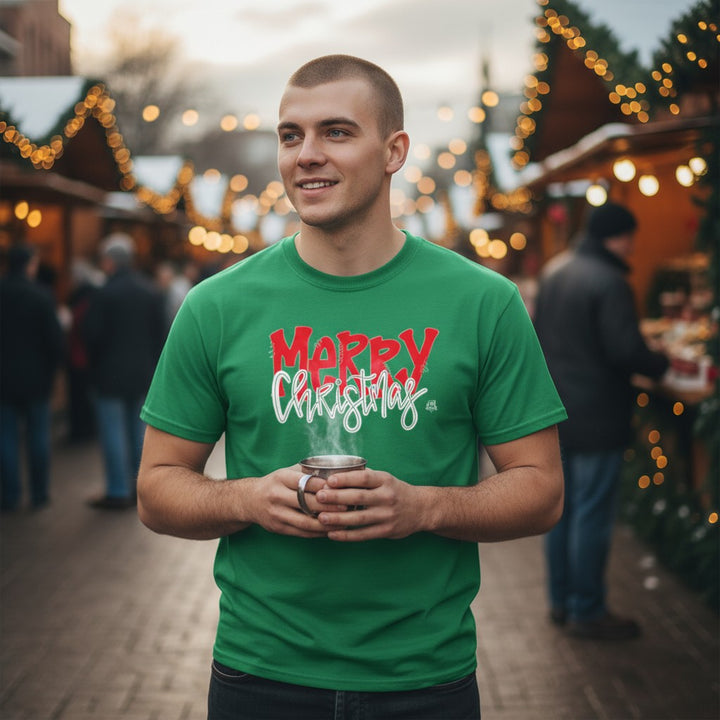 A smiling man wearing a green "MERRY Christmas" t-shirt while holding a mug at a holiday market.