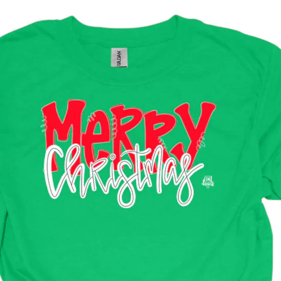 A close-up of the "MERRY Christmas" graphic on a green t-shirt, showing the baseball-style font.