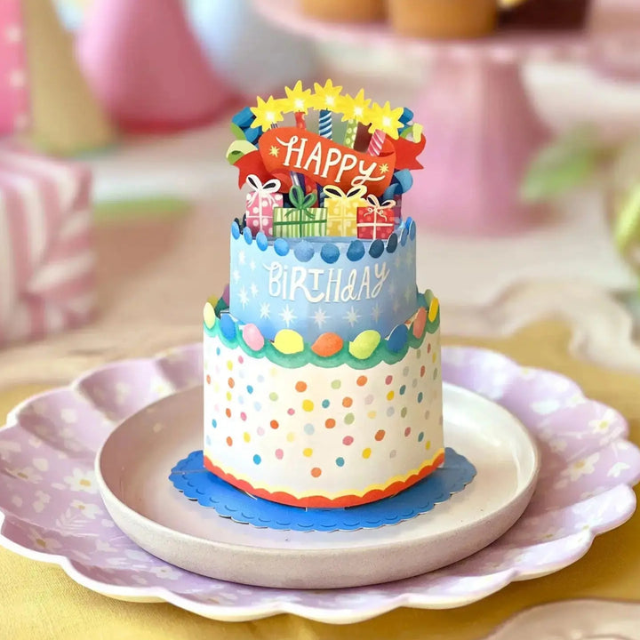 Colorful birthday cake with polka dots and 'Happy Birthday' toppers on a decorative plate.