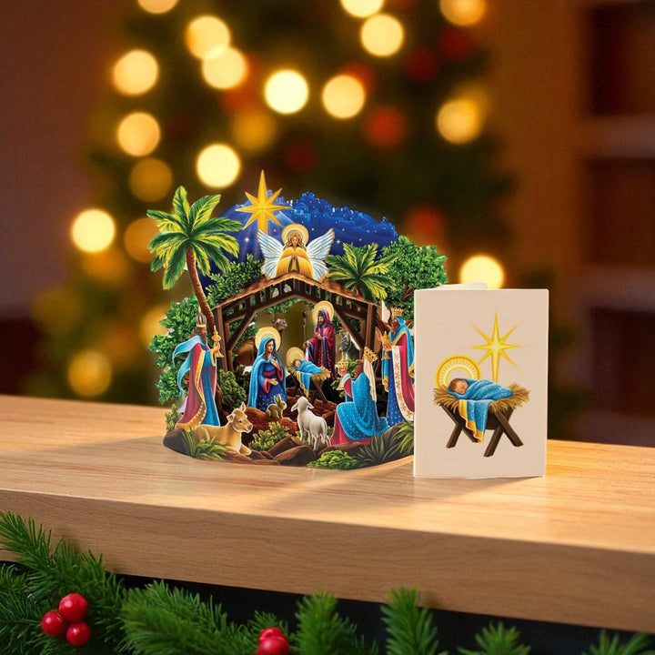 3D nativity scene with a card on a wooden surface in front of a blurred Christmas tree.