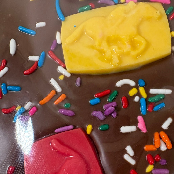 A close-up view of the yellow and red relief-molded horse candies resting on a rich milk chocolate slab covered in colorful sprinkles.