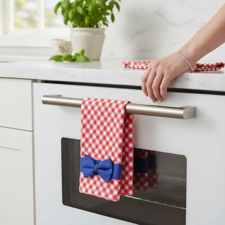 Red and white gingham tea towel with a blue bow hanging beautifully on a white kitchen oven handle next to marble countertops.