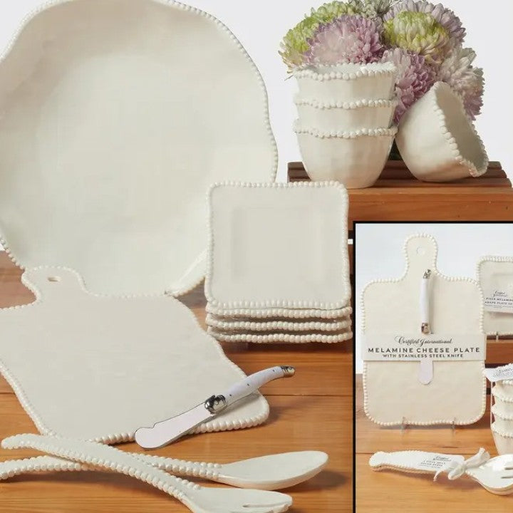 Set of white melamine cheese plates with matching cutlery on a wooden surface.