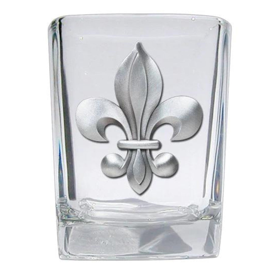 Clear glass shot glass with silver fleur-de-lis design on a white background