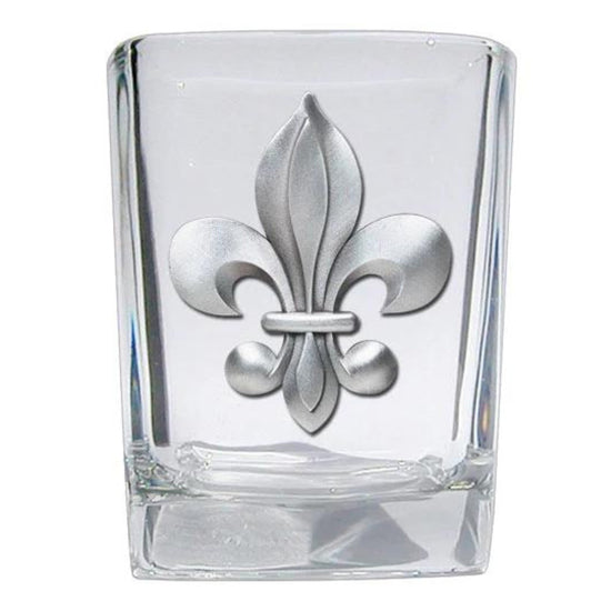 Clear glass shot glass with silver fleur-de-lis design on a white background