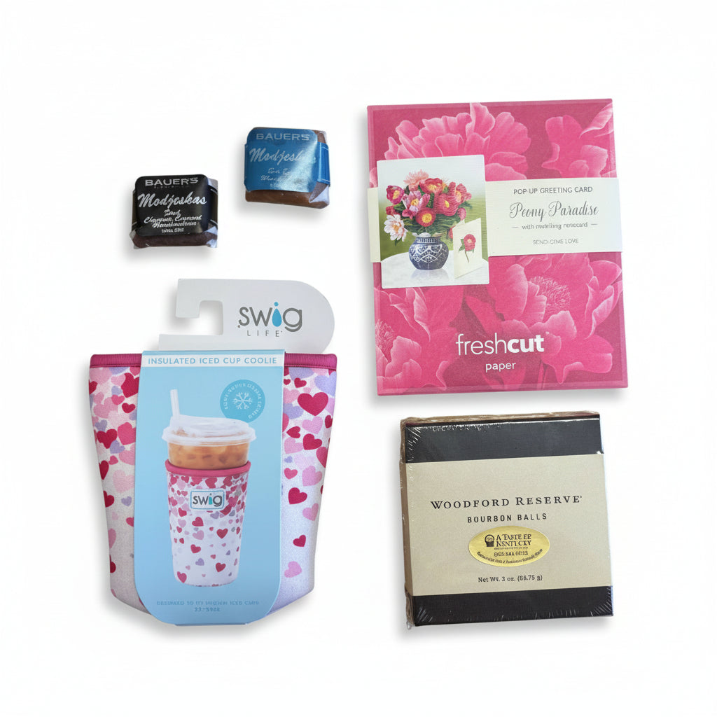 Top-down view of the basket contents: Swig Coolie, floral pop-up card, bourbon balls, and Modjeskas.