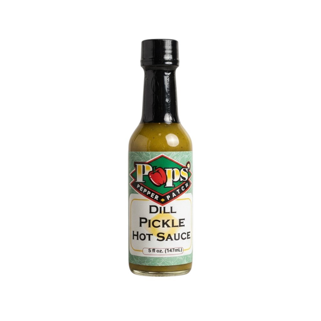 A 5oz glass bottle of Pops' Pepper Patch Dill Pickle Hot Sauce surrounded by fresh dill, garlic cloves, and jalapeños.