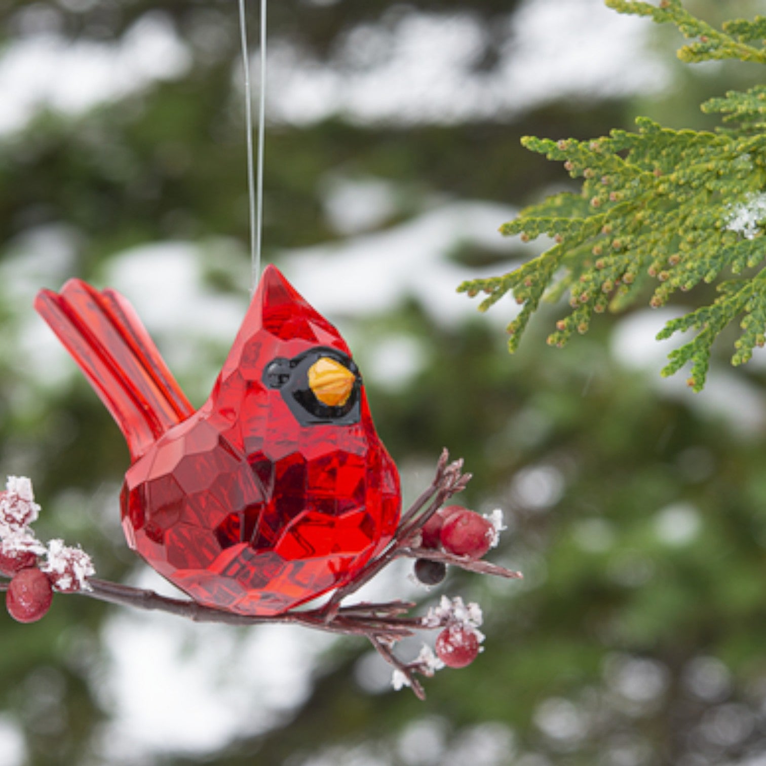 The elegant cardinal ornament hanging from a frosted branch with red berries.