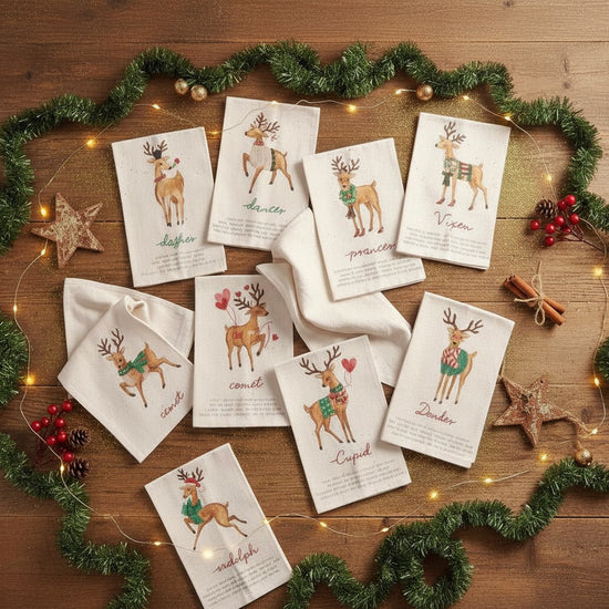 Set of Christmas-themed poem tea towels with reindeer illustrations on a wooden surface with festive decorations.