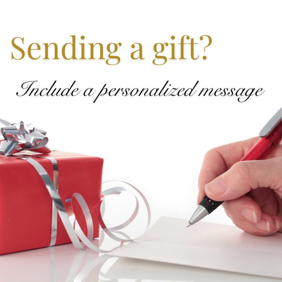 Red gift box with silver ribbon and hand writing a personalized message on a white surface.